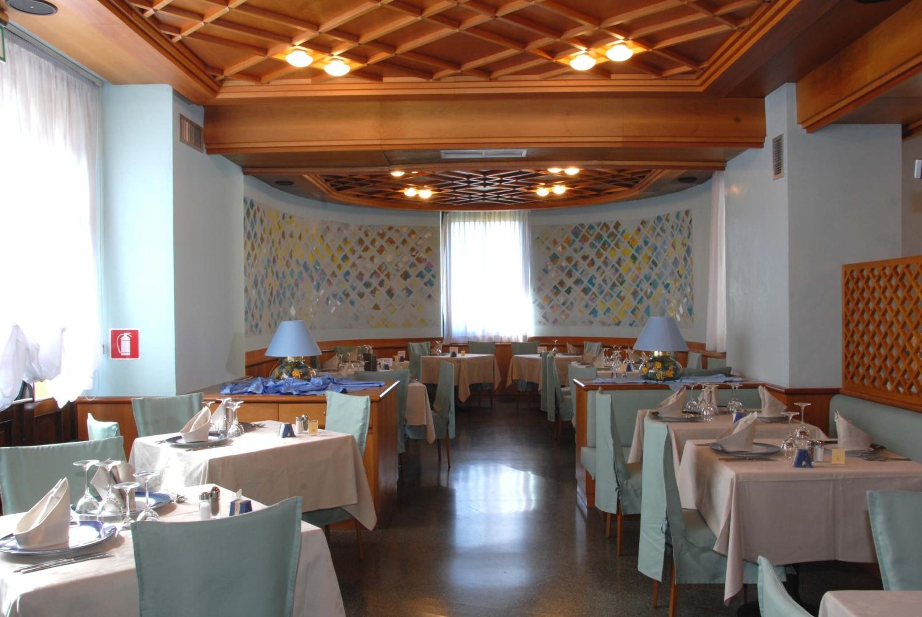 A dining area with tables set for service, wooden ceiling beams, and patterned wallpaper.