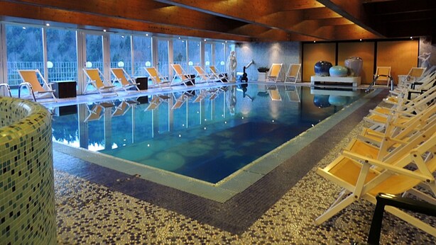 An indoor swimming pool with clear water, surrounded by lounge chairs and a tiled floor. - Grand Hotel Astoria (Lavarone)