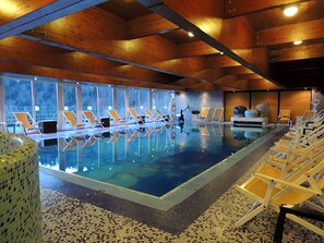 Una piscina interior con agua cristalina, rodeada de sillones de descanso y un suelo de baldosas.