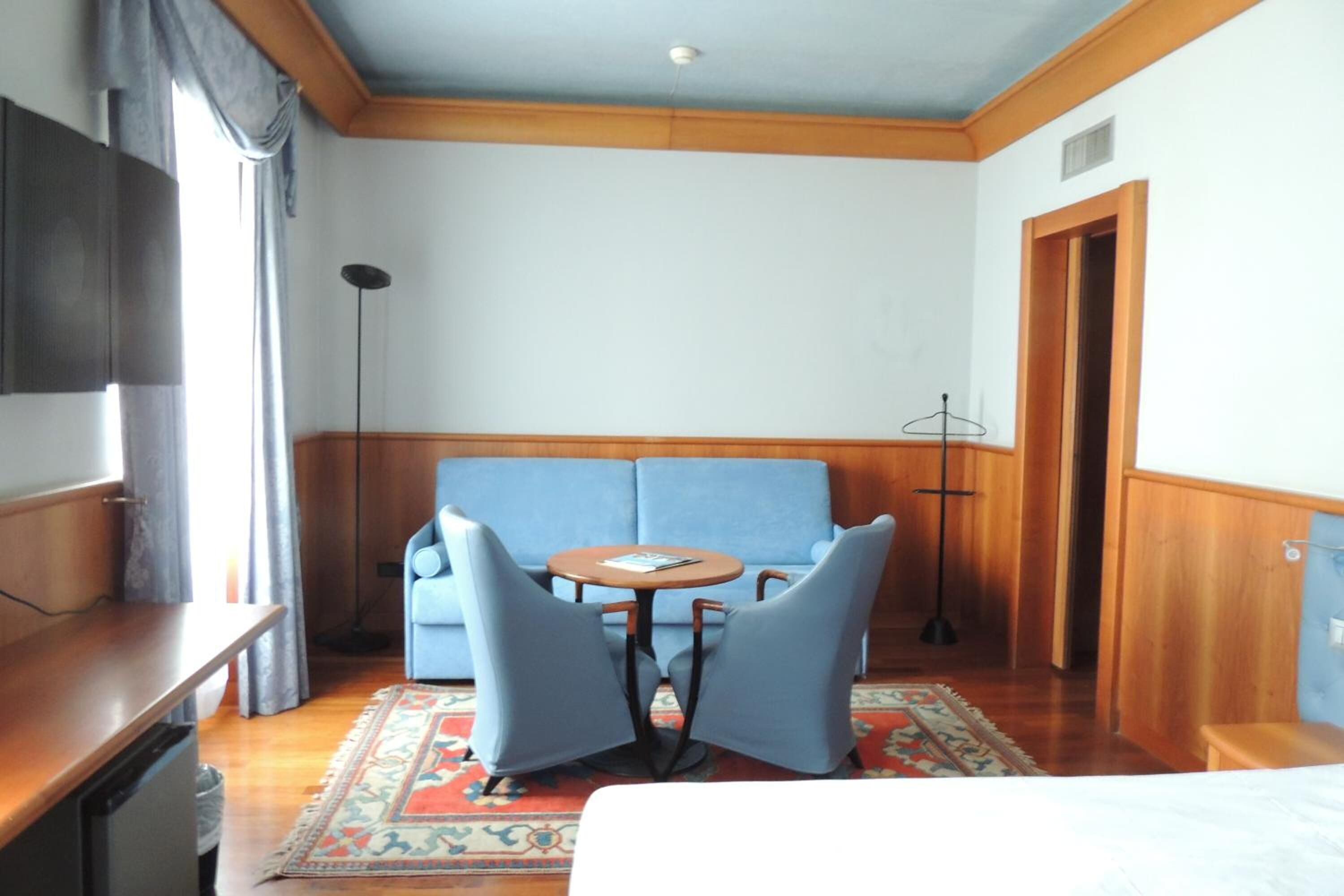 A room with a blue sofa, a small round table, a TV, and a wooden floor.