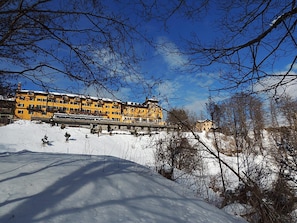 A multi-story yellow building with a snow-covered landscape and bare trees in the foreground.