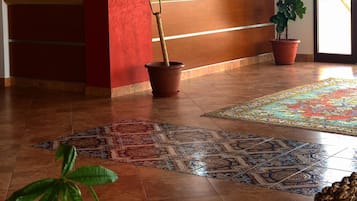 Un'area reception con una parete rossa, una scrivania in legno, due piante in vaso, un tappeto decorato e un orologio a parete.