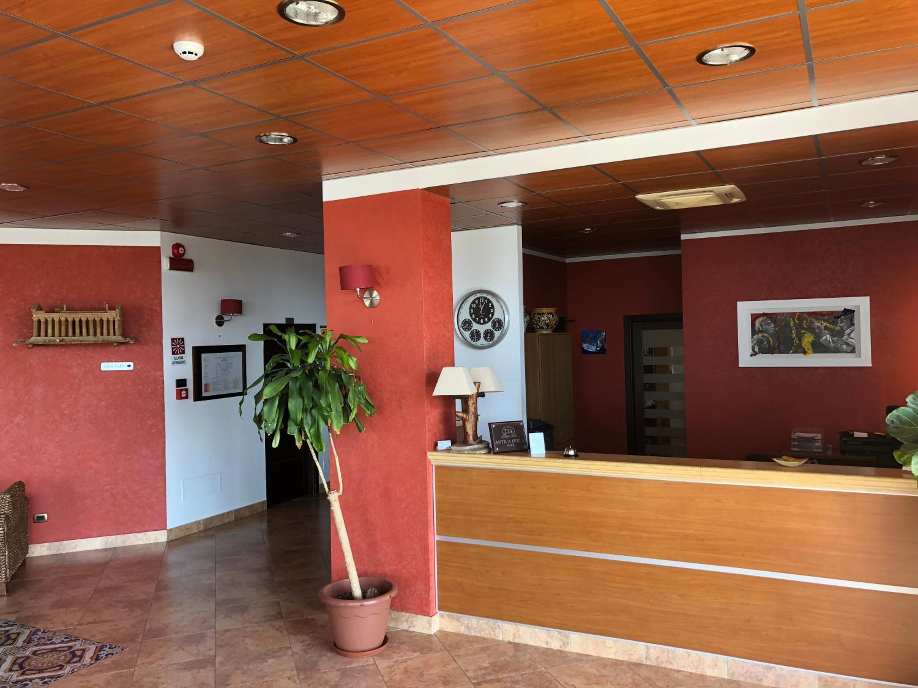 A reception area with a wooden reception desk, a potted plant, a wall clock, and a framed artwork.