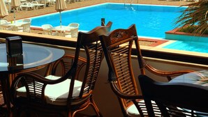 Zona junto a la piscina con sillas de descanso blancas y sombrillas, una mesa de madera y vistas al océano.