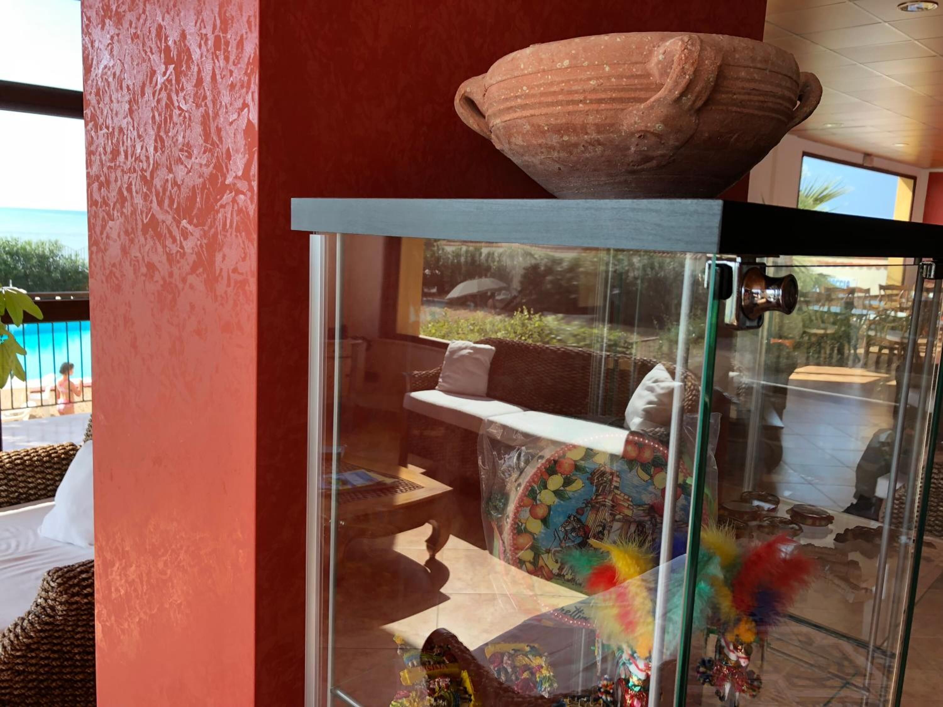 Una habitación con una vitrina que contiene objetos decorativos, un sofá de mimbre y vistas a una piscina exterior.