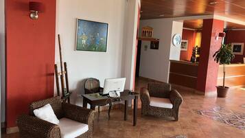 Un hall d’entrée avec des meubles en osier, un bureau avec un ordinateur, un tableau accroché au mur et, au fond, un espace d’accueil.