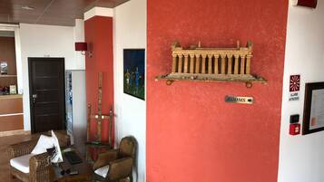 A lobby with a red accent wall, a wooden bench, a wicker sofa, a small table with a keyboard, and a sign indicating 'ROOMS'.