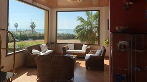 Una habitación con muebles de mimbre, ventanas amplias y vista al mar.