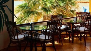 Una terraza con sillas y mesas de madera, con vistas a una palmera y al mar.