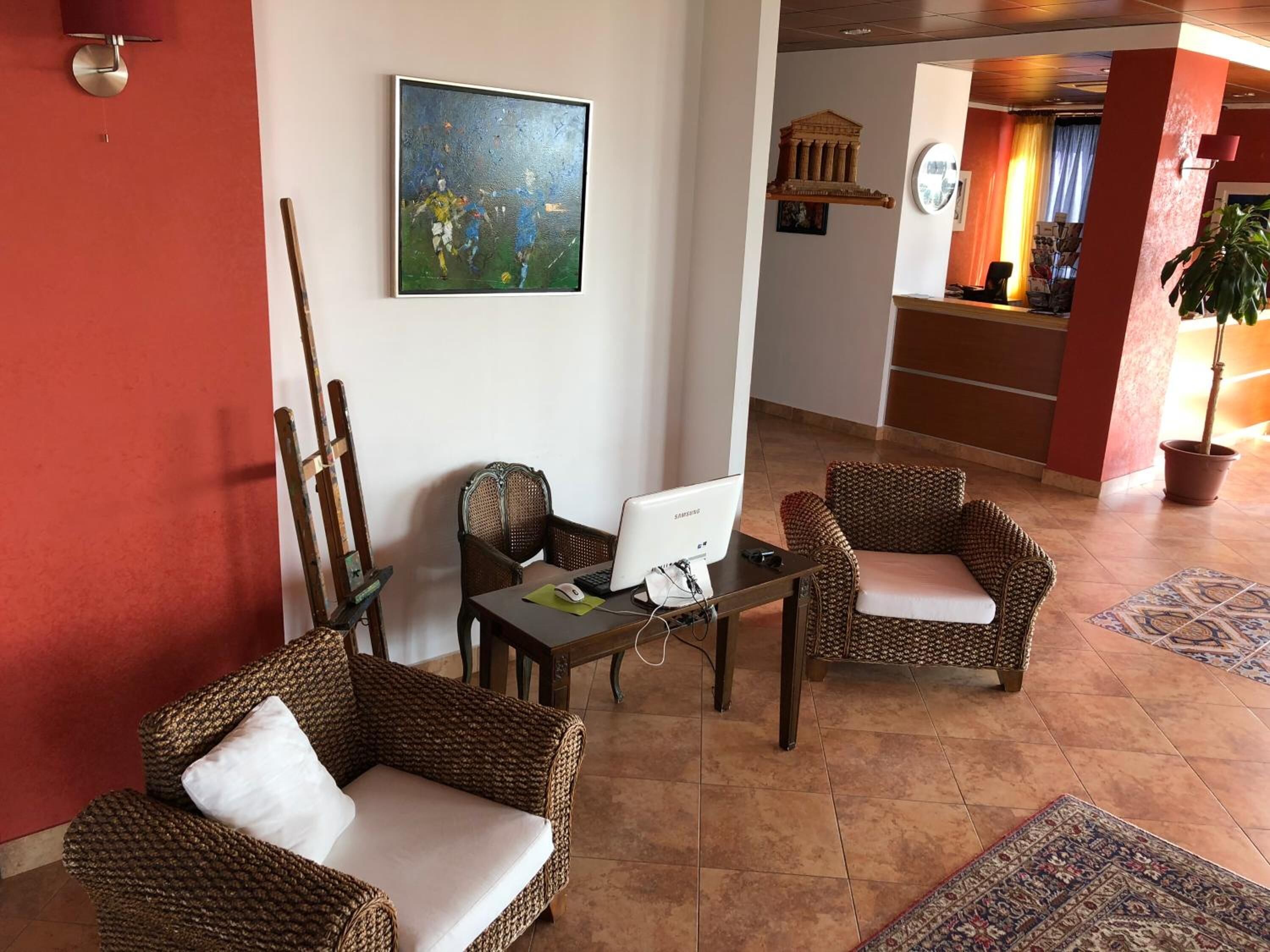 A lobby with wicker furniture, a desktop computer, and a painting on the wall.