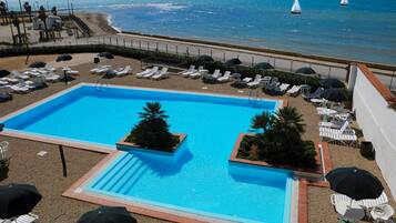 Piscina con sillones de playa y sombrillas, con vista a la playa.