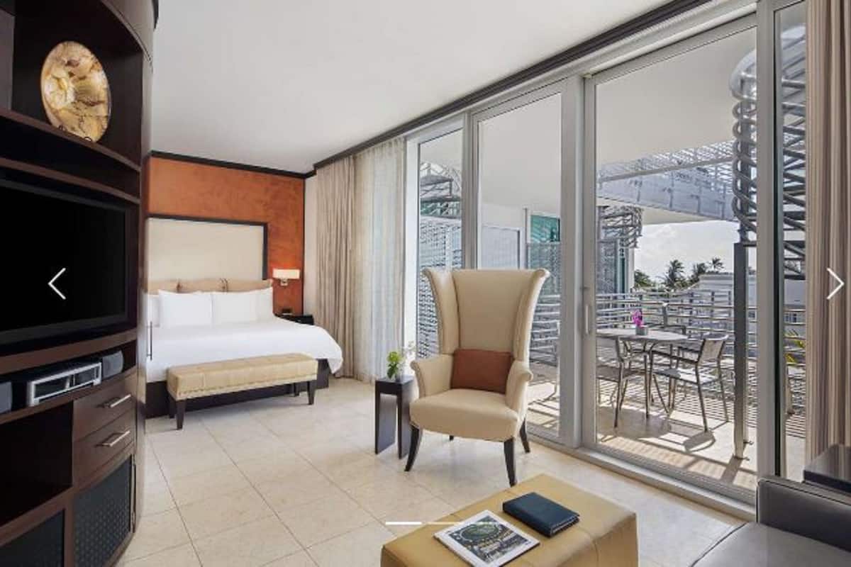 Une chambre d’hôtel comprenant un lit, une chaise, une télévision, une table basse et un balcon avec une table et des chaises.