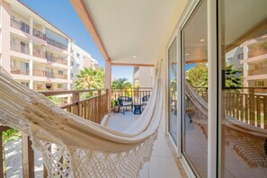 A balcony with a hammock, a table, and chairs, overlooking a building with multiple balconies and palm trees. - Beach Park Wellness Resort (Aquiraz)