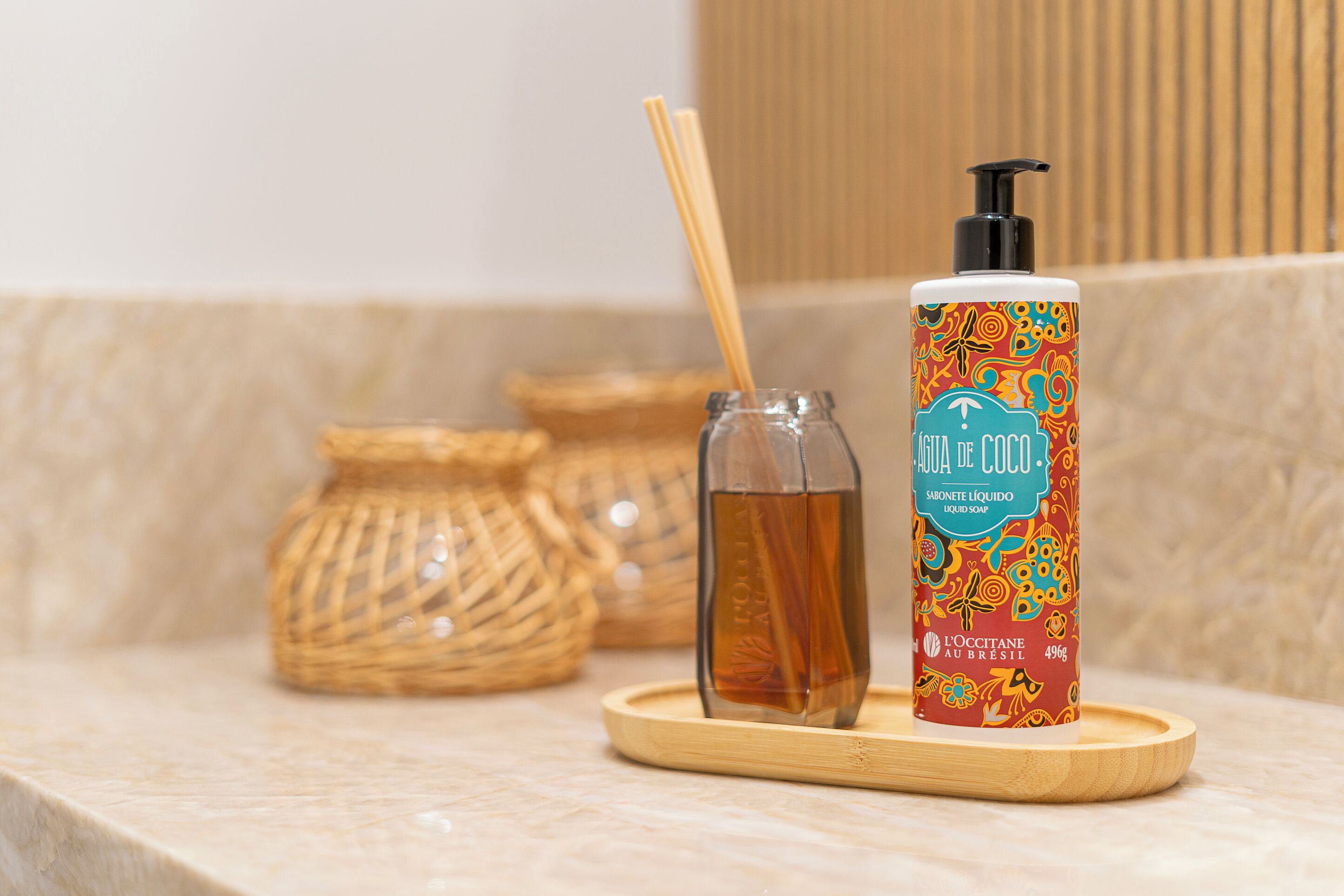 A bottle of L'OCCITANE AU BRASIL soap on a wooden tray with a glass bottle and a bamboo stick.