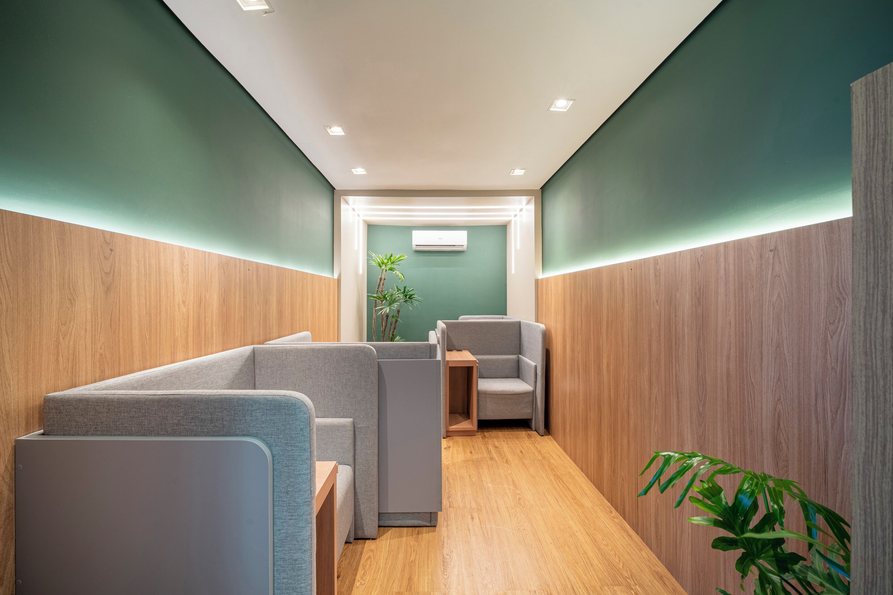 A modern waiting area with wooden paneling, grey seating, and a plant.
