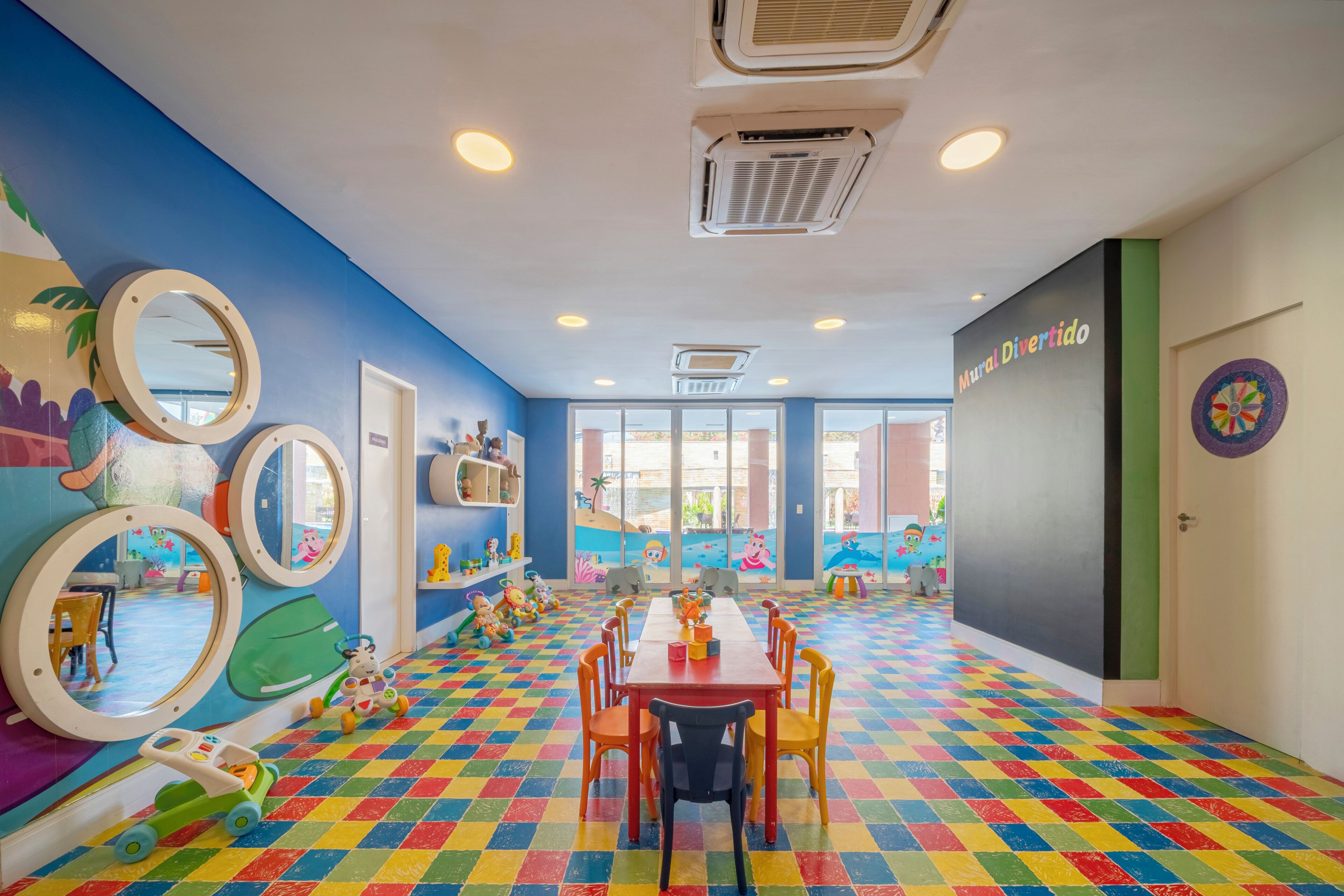 A vibrant children's playroom with colorful checkered flooring, a long table, and playful wall decorations.