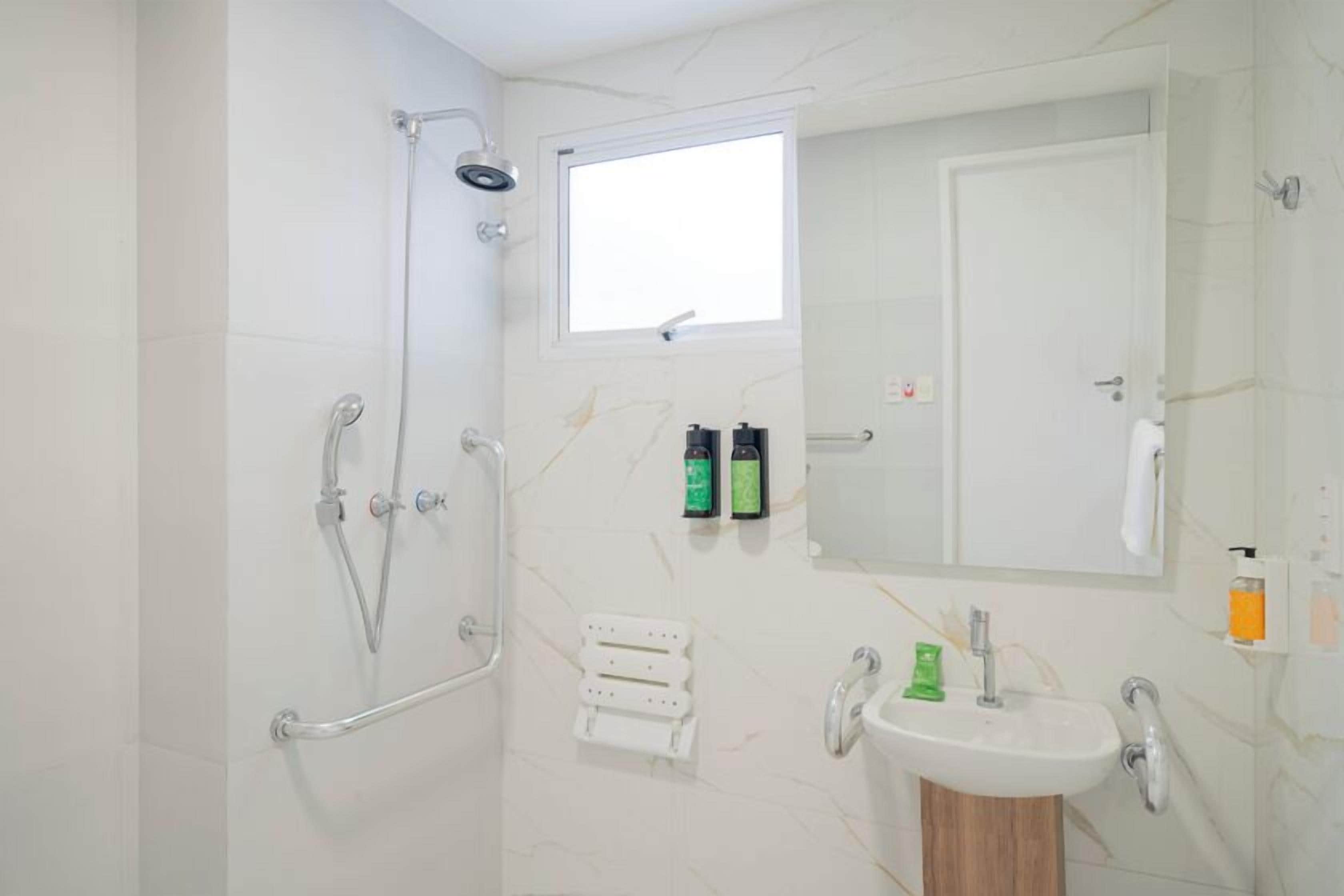 Une salle de bain avec une douche, un lavabo, un miroir et une fenêtre.
