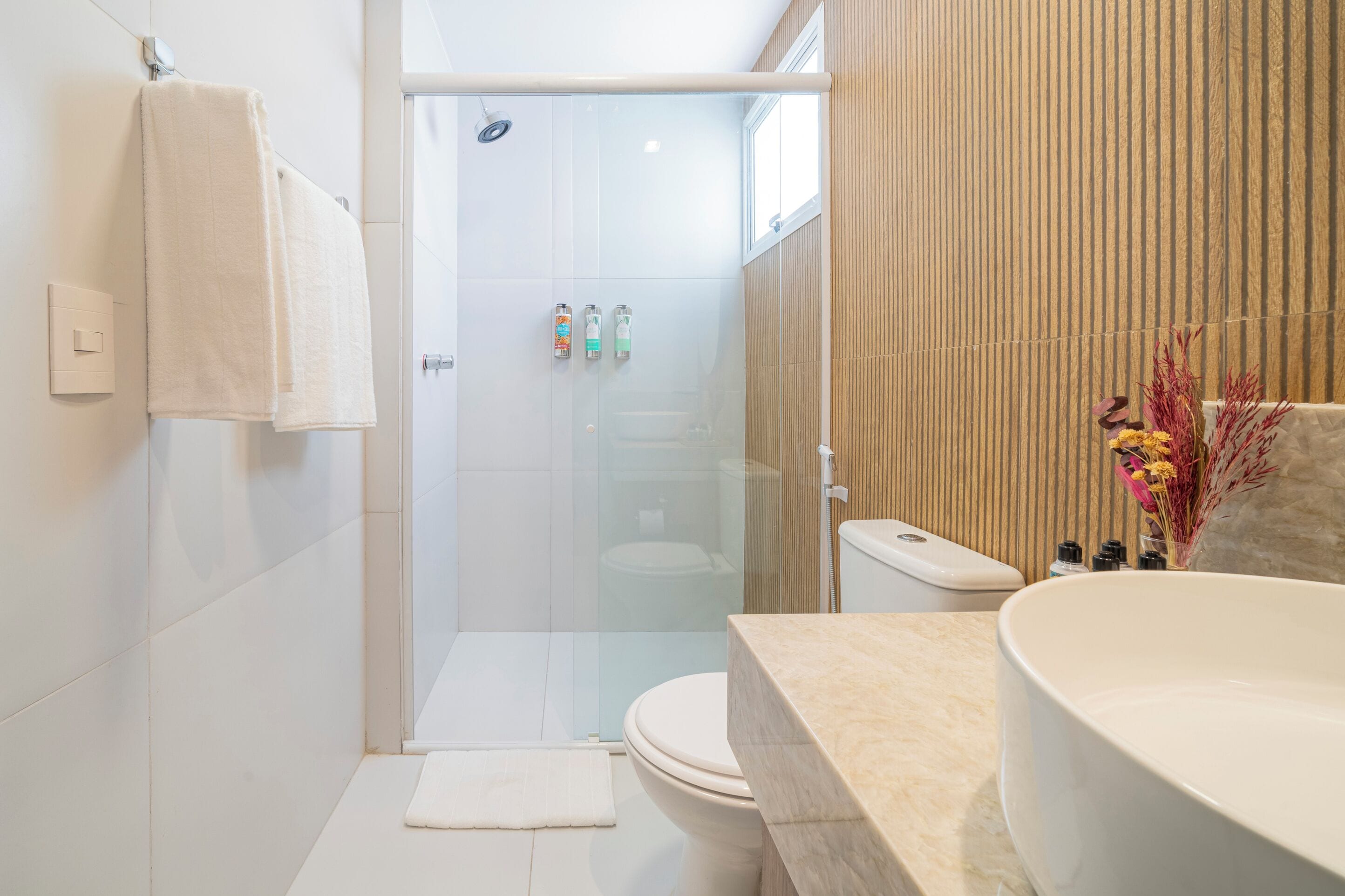 A modern bathroom with a glass-enclosed shower, a toilet, and a large sink with a beige countertop.