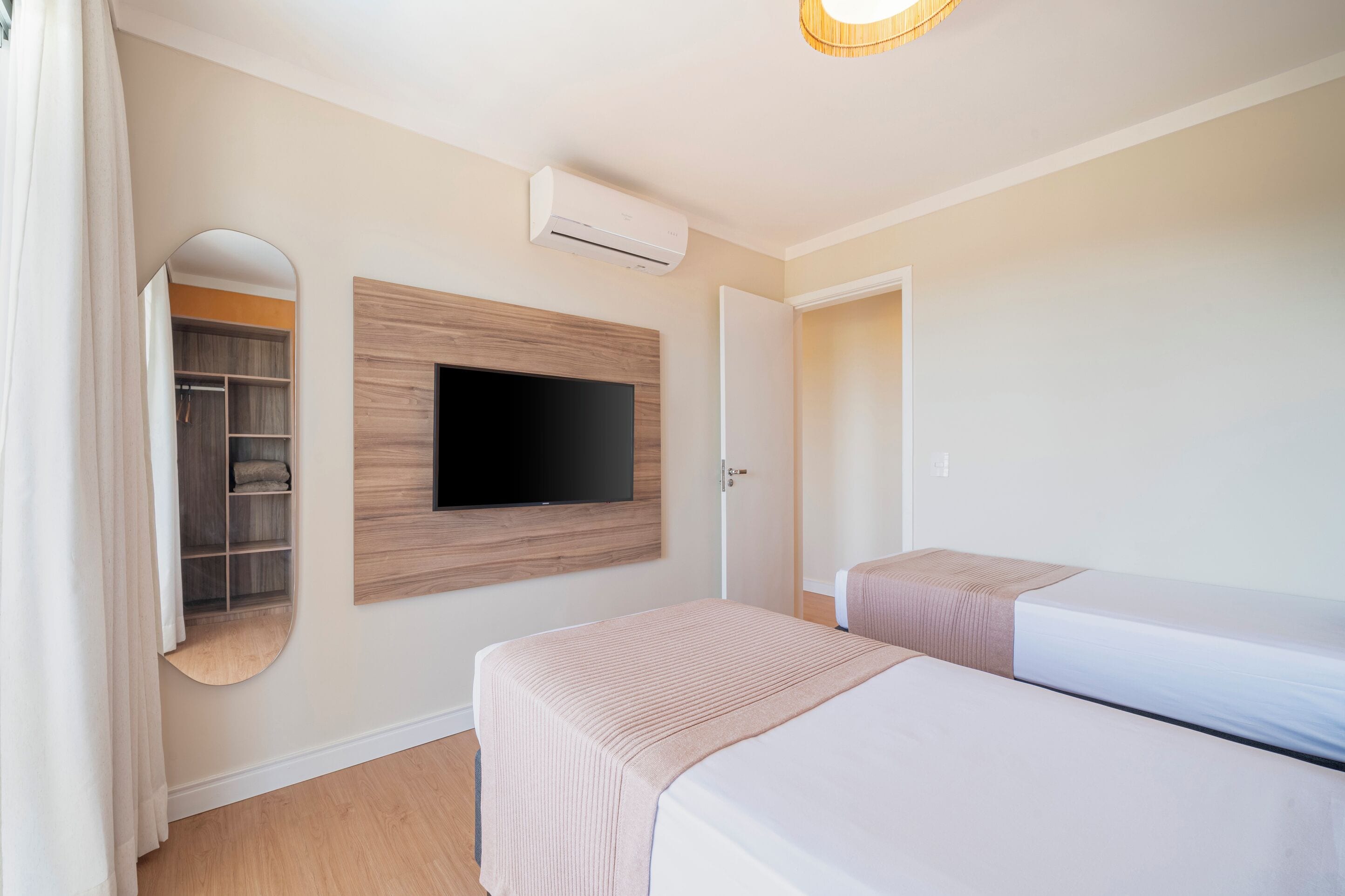 Habitación de hotel con dos camas, un televisor montado en la pared, un armario y un equipo de aire acondicionado.