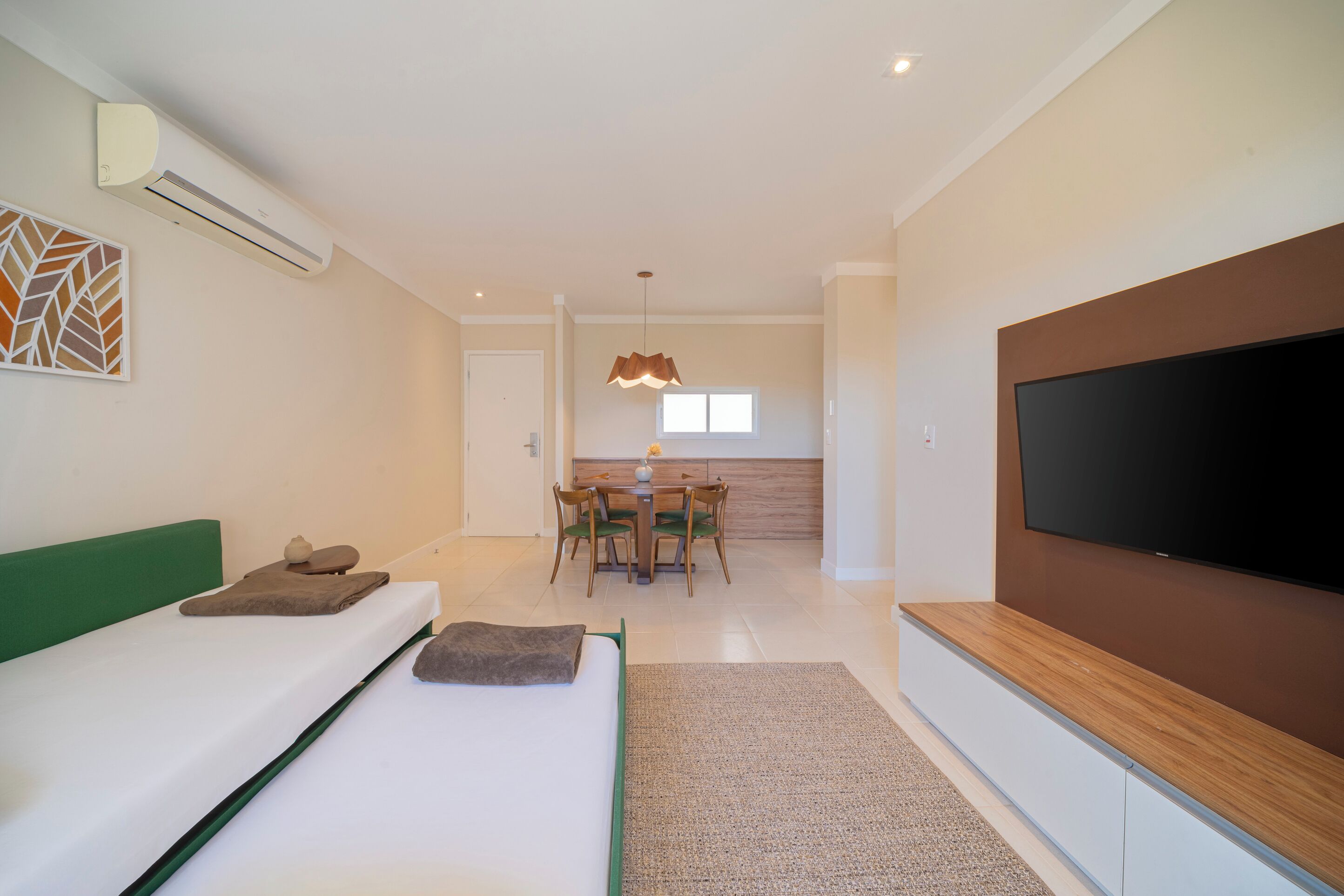 A modern hotel room with a bed, a TV, a dining area, and an air conditioning unit.
