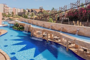 A large outdoor swimming pool with a water slide, surrounded by palm trees and a wooden bridge. - Beach Park Wellness Resort (Aquiraz)
