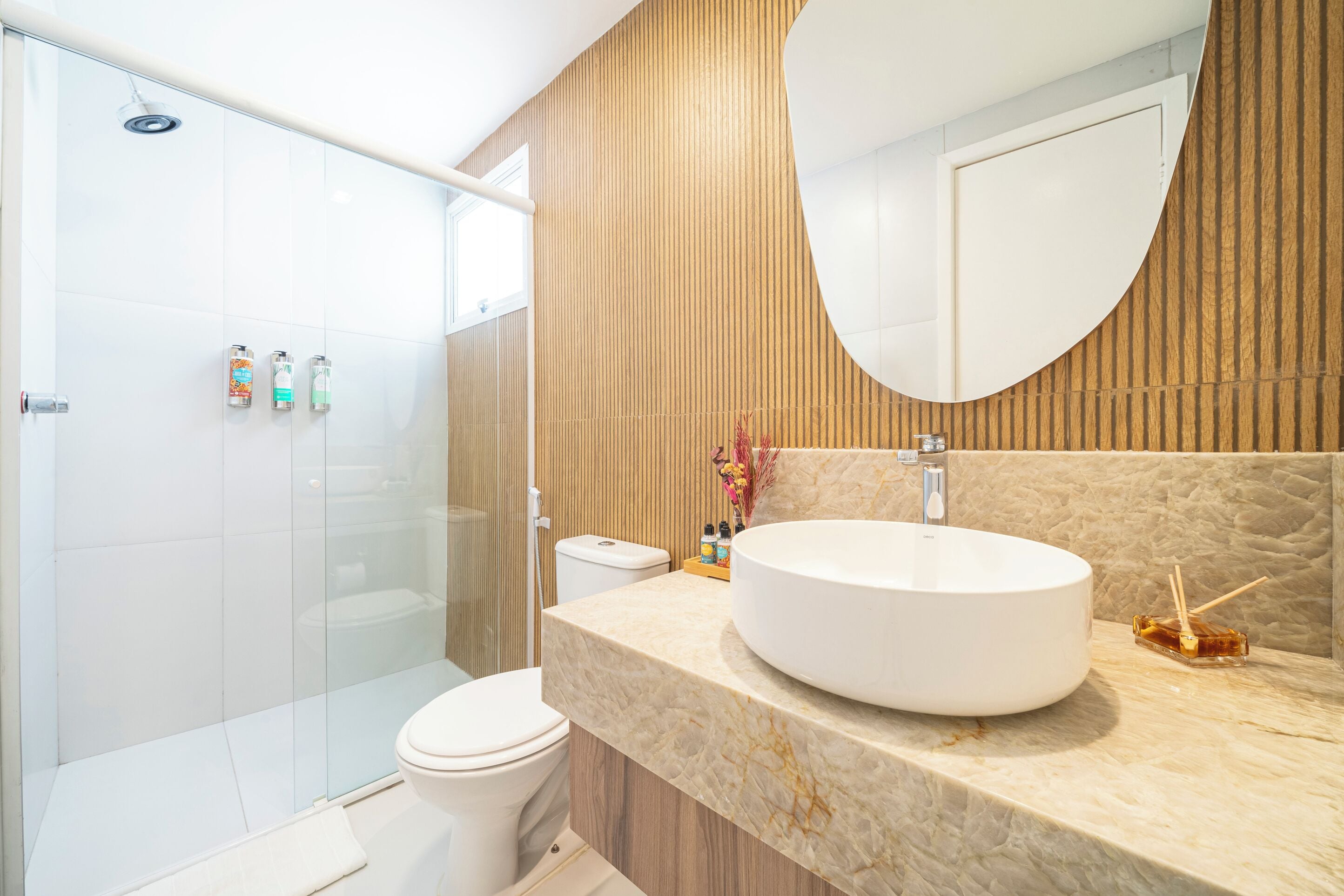 A modern bathroom with a glass shower enclosure, a white toilet, and a large oval sink with a wooden vanity.