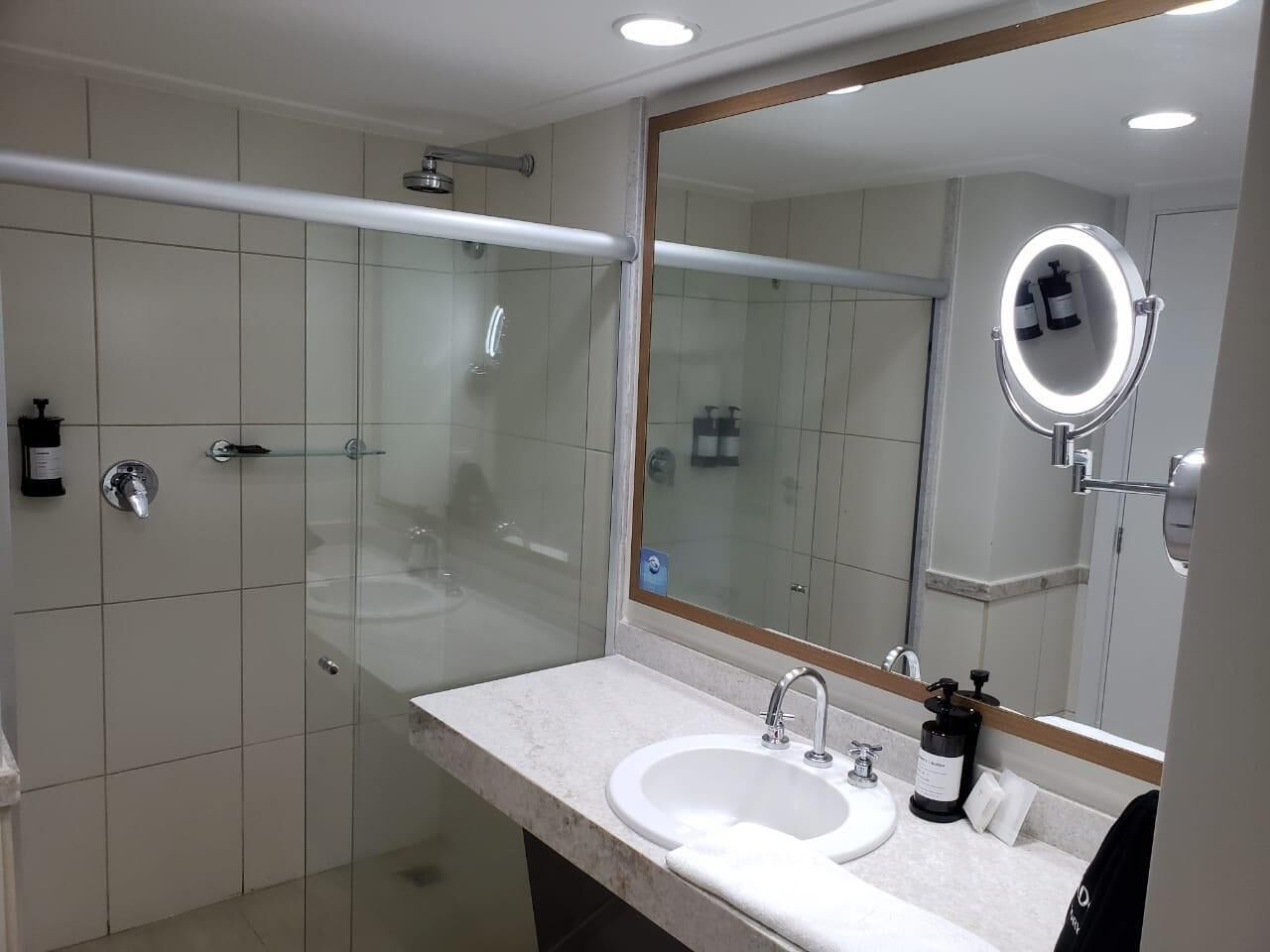 A modern bathroom with a glass-enclosed shower, a white sink, and a mirror with a light.