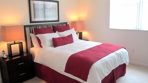A neatly made bed with a white and red bedspread and pillows, flanked by two bedside tables with lamps. - Churchill Suites Miami Brickell (Miami)