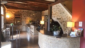 Un interior rústico con barra de piedra, vigas de madera en el techo y una escalera adosada a un muro de piedra.