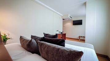 A modern hotel room with a large bed, dark brown pillows, a small desk, and a flat-screen TV mounted on the wall.