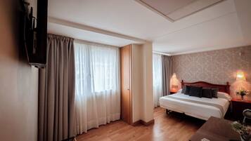 A hotel room with a bed, bedside tables, a TV mounted on the wall, and a wooden floor.