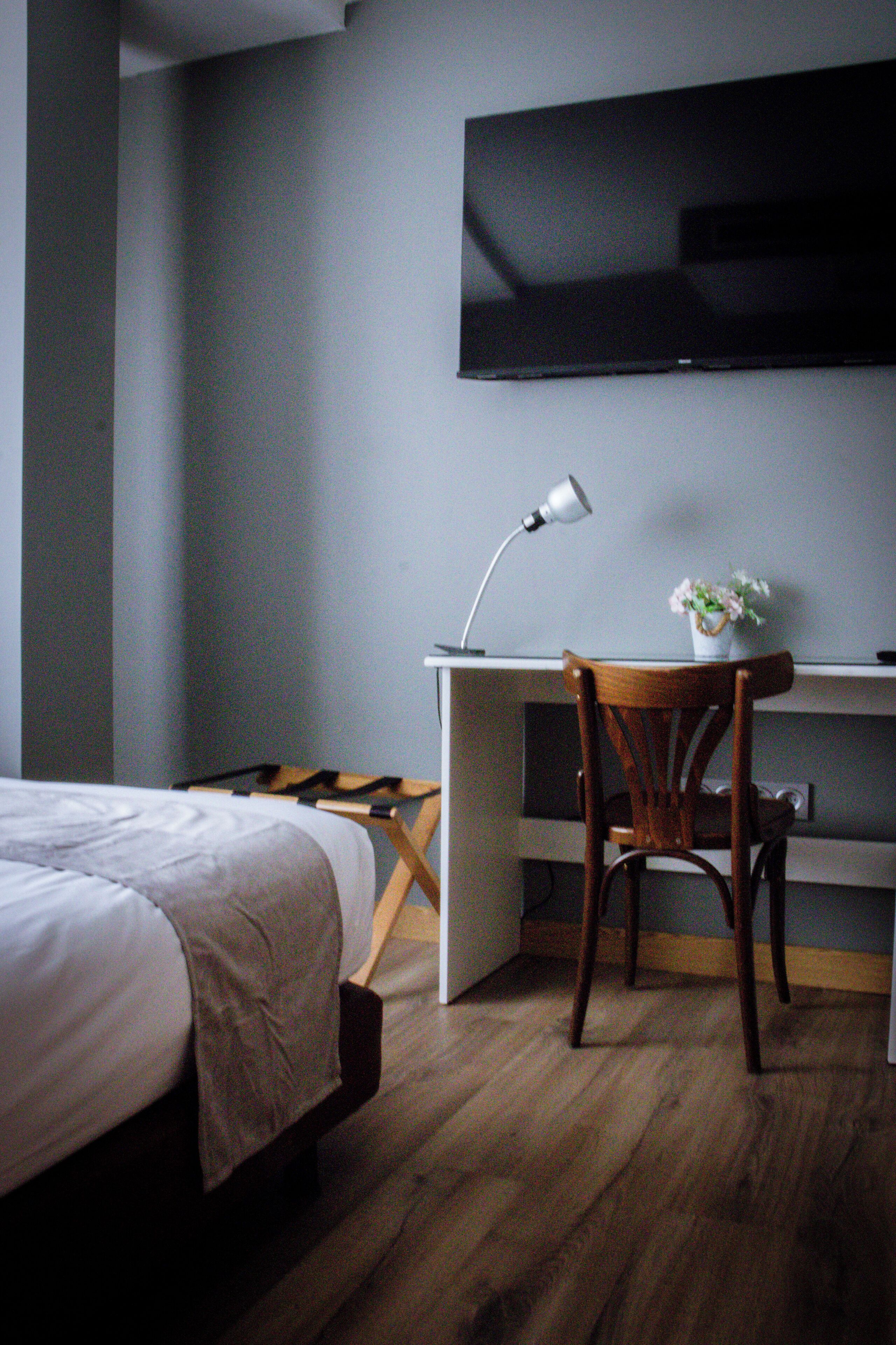 Un dormitorio con una cama, un escritorio con silla, un televisor montado en la pared y una lámpara en el escritorio.