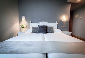 A neatly made bed with white linens and two pillows, a bedside table with a lamp, and a wall-mounted light fixture.
