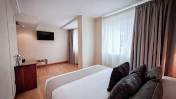 Een hotelkamer met een groot bed, een bureau met spiegel en een flatscreen televisie aan de muur.