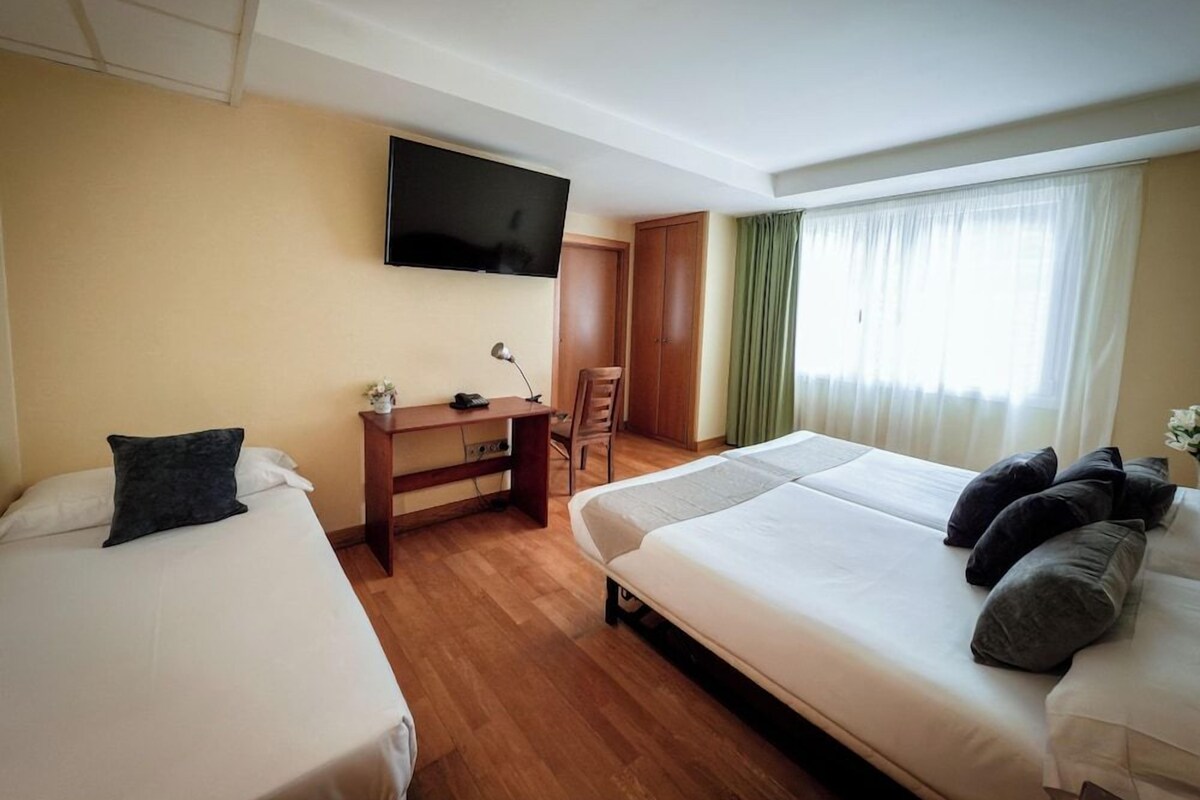 A hotel room with two beds, a desk, a TV, and a window with curtains.