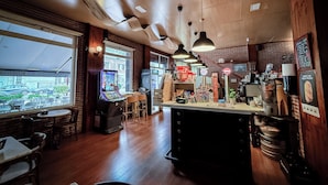 Een restaurant met een bar, houten vloeren en een uitzicht op de straat door grote ramen.