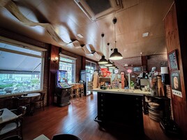 A restaurant with a bar area, wooden flooring, and a view of the street through large windows.