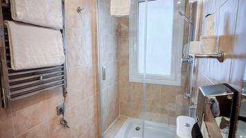 A modern bathroom with a glass-enclosed shower, a toilet, and a towel rack with folded towels.