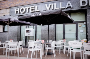 An outdoor seating area with tables and chairs in front of a building with a sign reading 'HOTEL VILLA DE LA SALVE.'