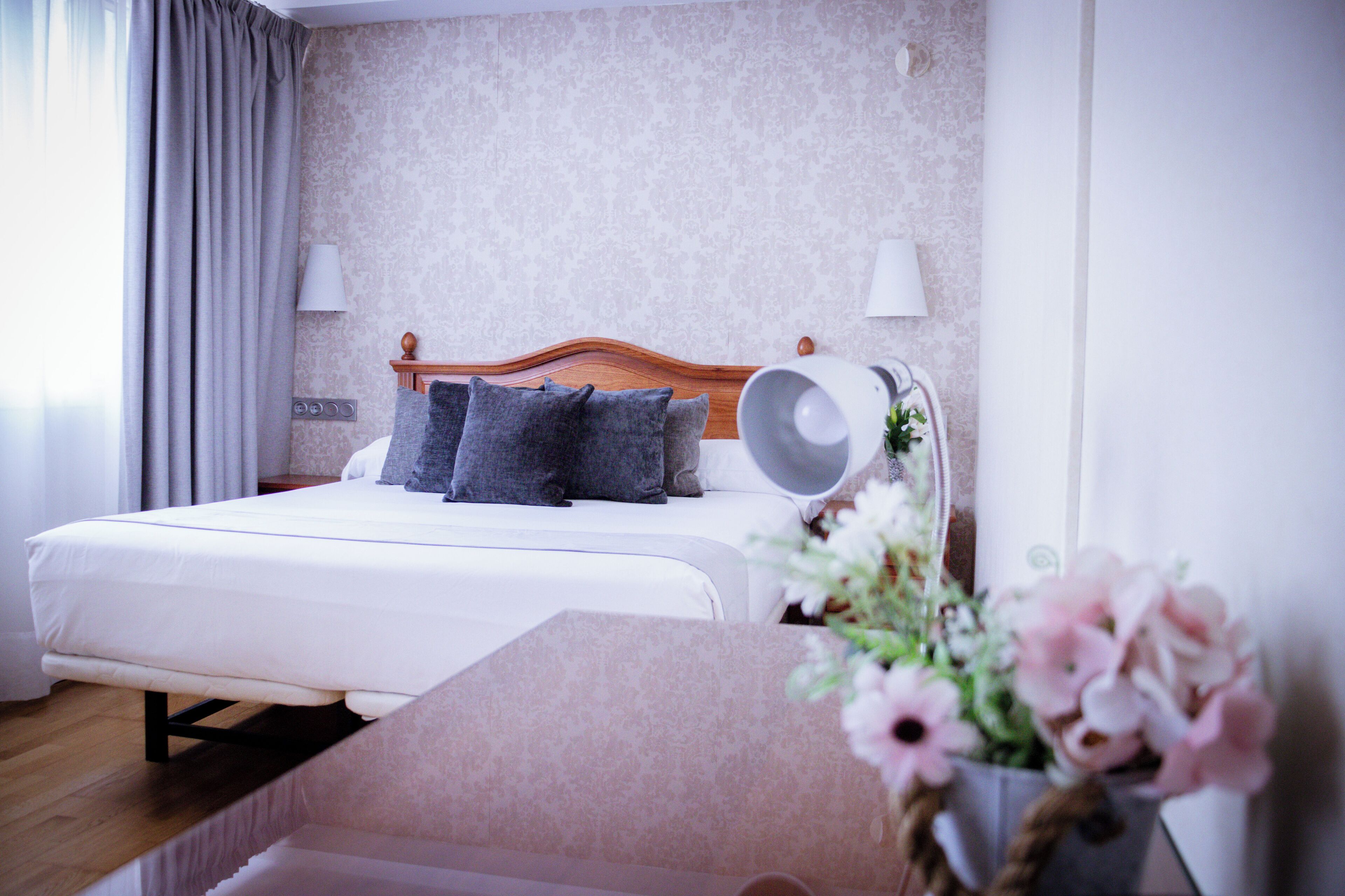 Une chambre d’hôtel avec un lit, des lampes de chevet, une tête de lit en bois et une plante en pot.