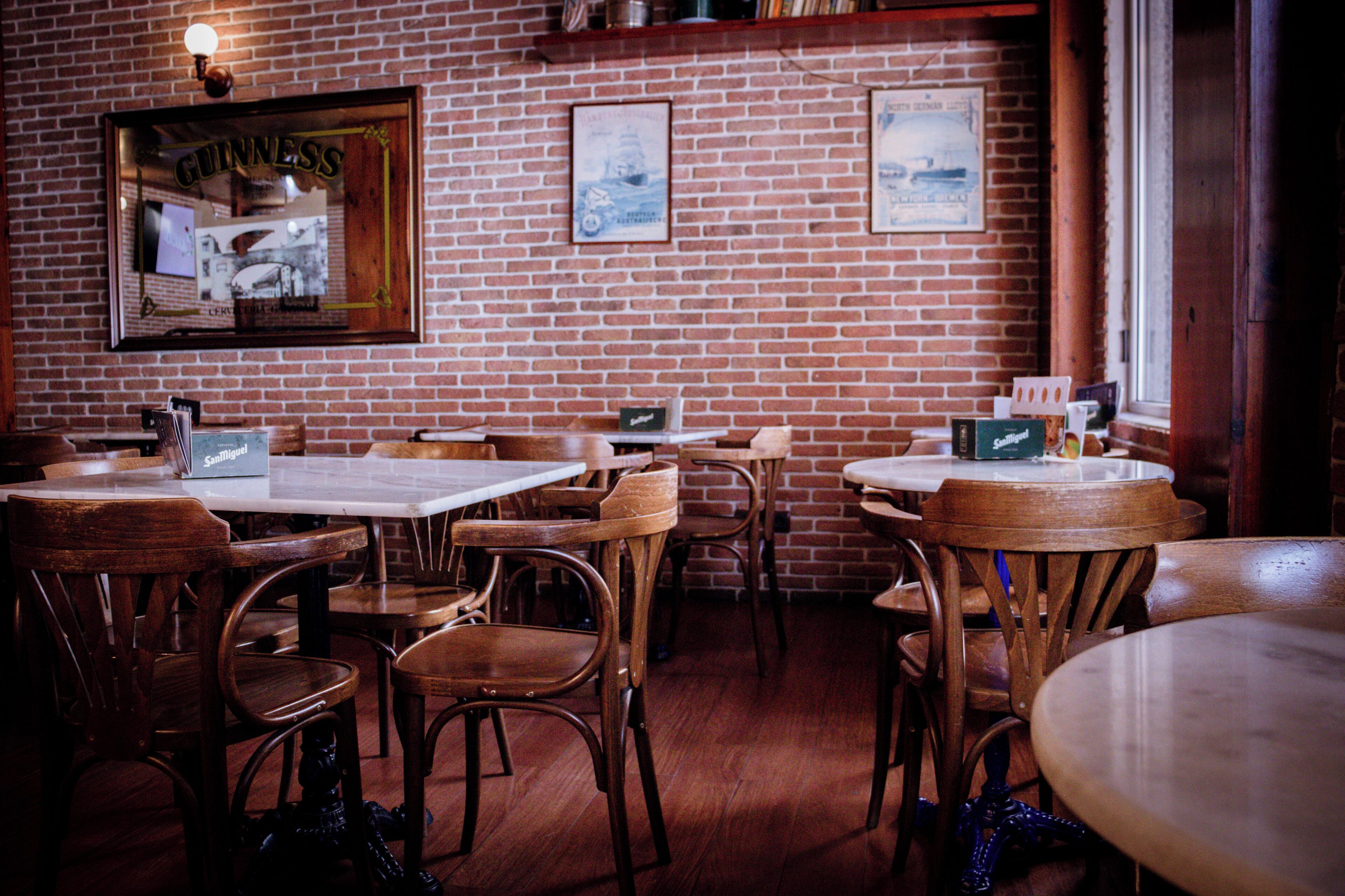 Interior de restaurante con paredes de ladrillo, mesas y sillas de madera, y cuadros en la pared.