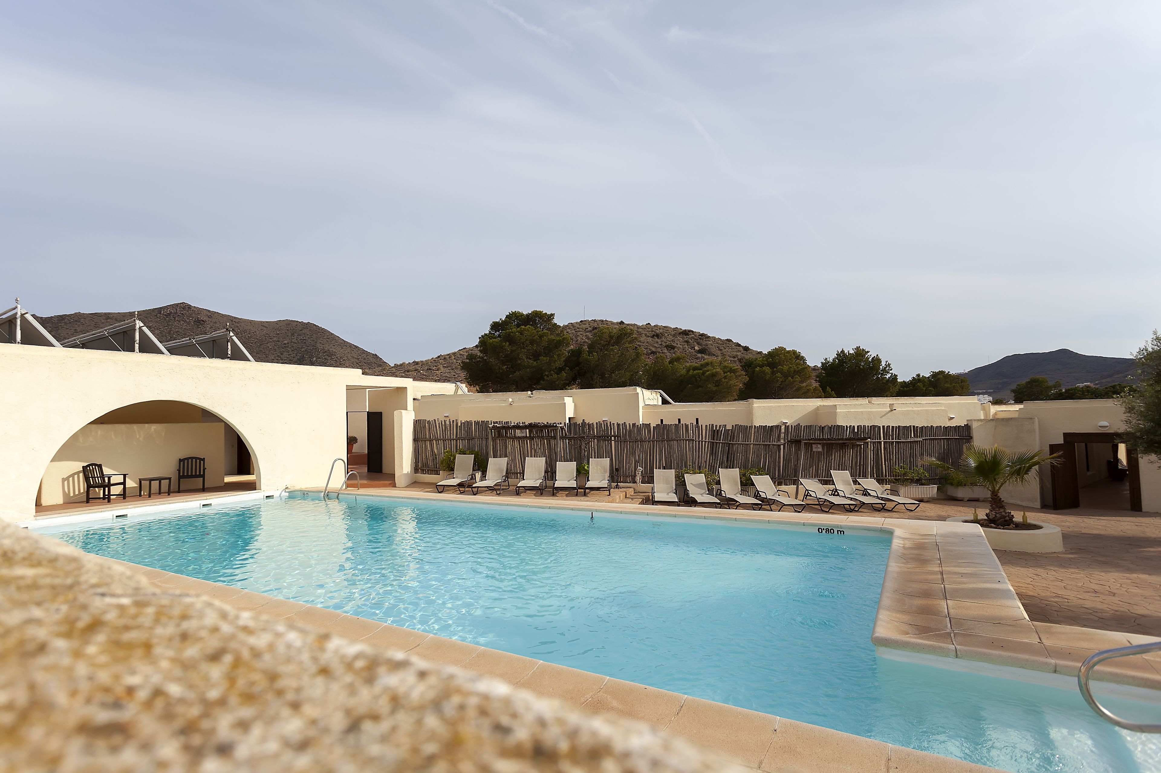 A swimming pool with lounge chairs and a covered seating area, surrounded by mountains.
