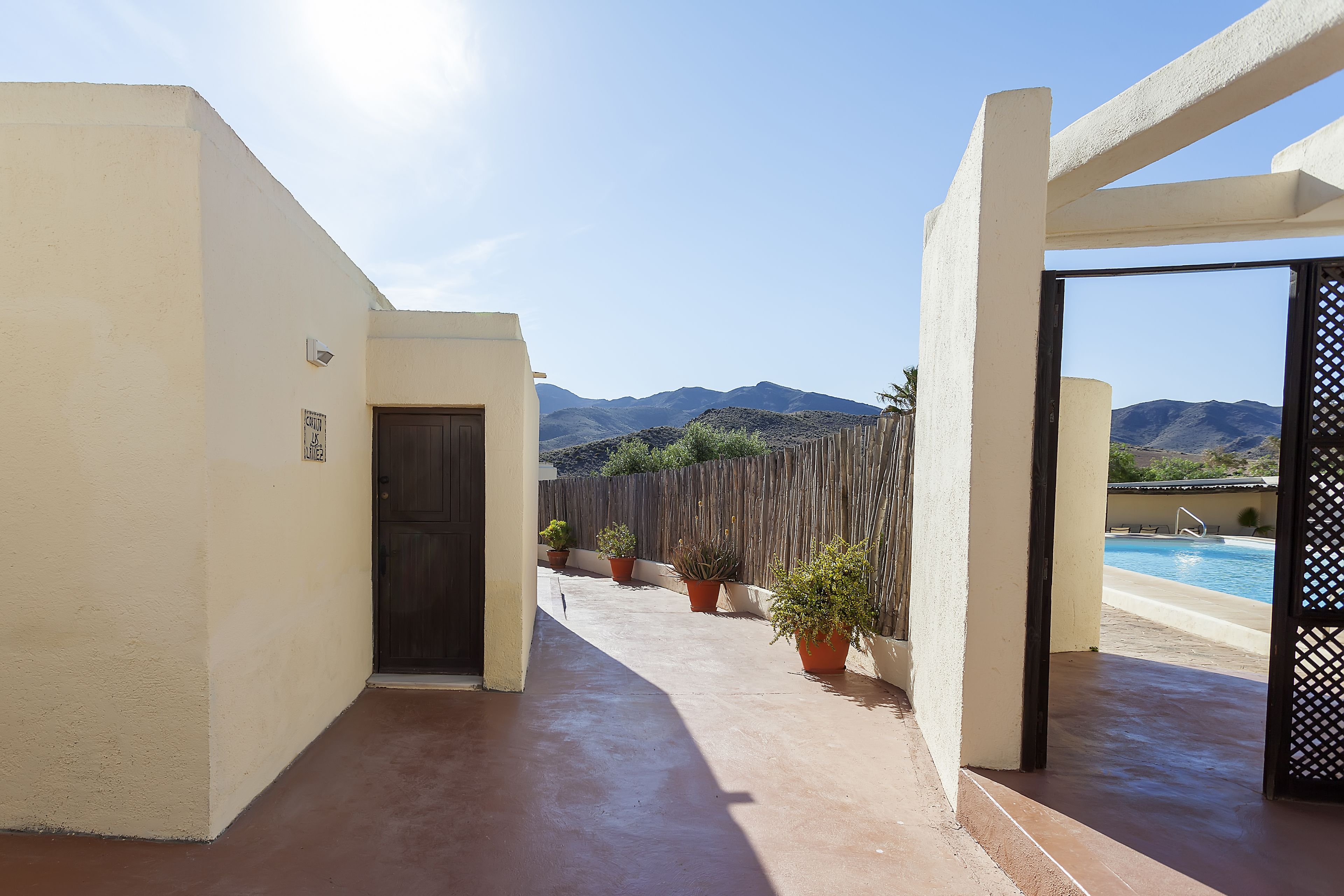 Un espacio exterior cubierto con piscina, plantas en macetas y montañas al fondo.