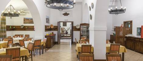 Comedor con varias mesas dispuestas para comensales, con candelabros y sillas de madera.