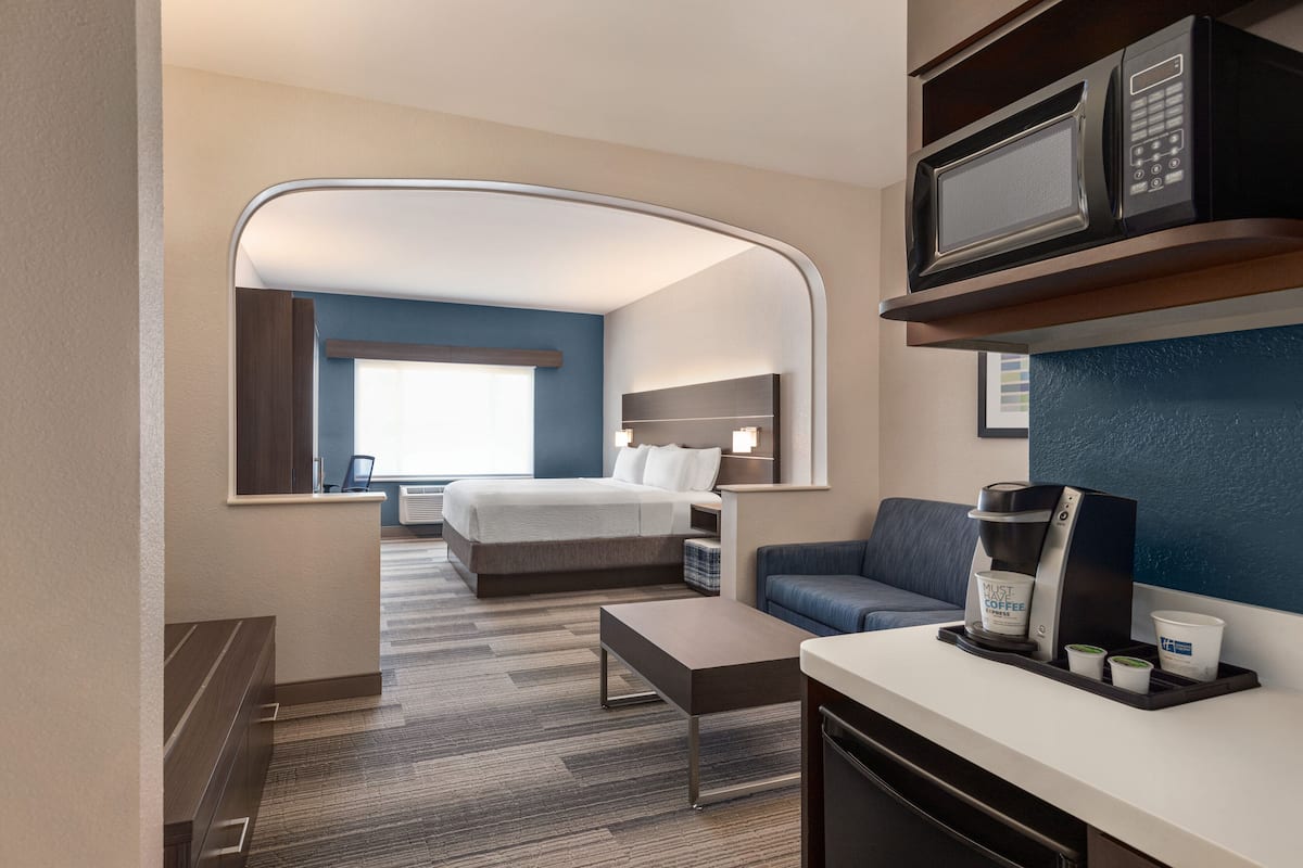 A hotel room with a bed, a sofa, a coffee station, and a microwave.