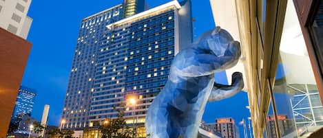 Un moderno edificio hotelero con una fachada de vidrio destacada y una gran escultura en primer plano.