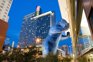 A modern hotel building with a prominent glass facade and a large sculpture in the foreground.