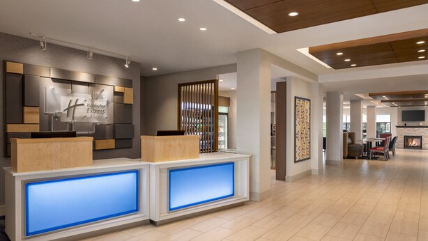 Zona de recepción de hotel con diseño moderno, que incluye un mostrador de recepción con paneles azules iluminados, un mostrador de madera y un letrero fijado a la pared.