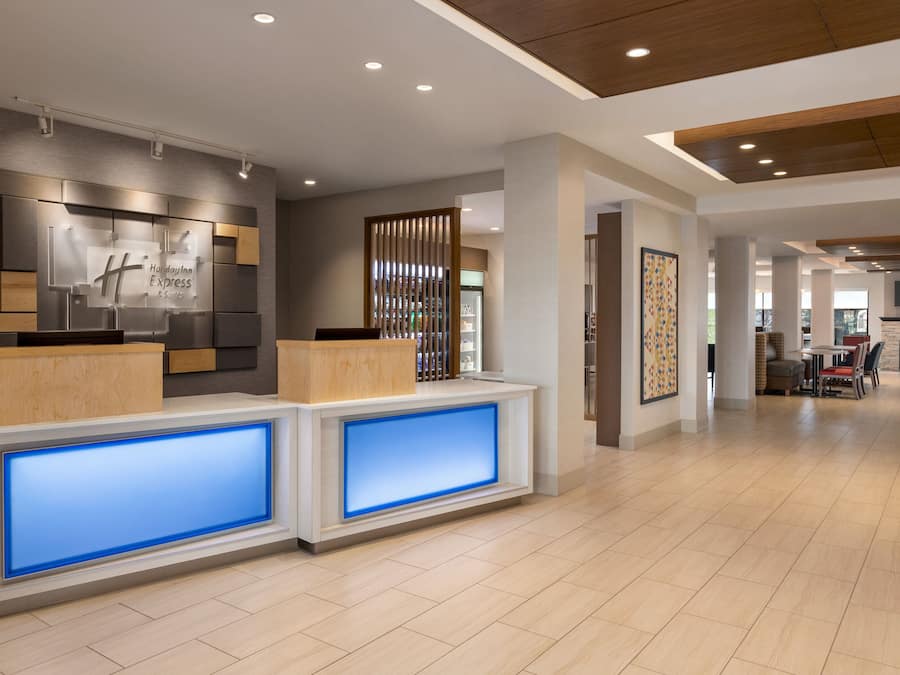 A hotel reception area with a modern design, featuring a reception desk with illuminated blue panels, a wooden reception desk, and a wall-mounted sign.