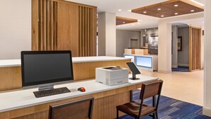 Un mostrador de recepción con una computadora, impresora y un pequeño espacio de espera con sillas.